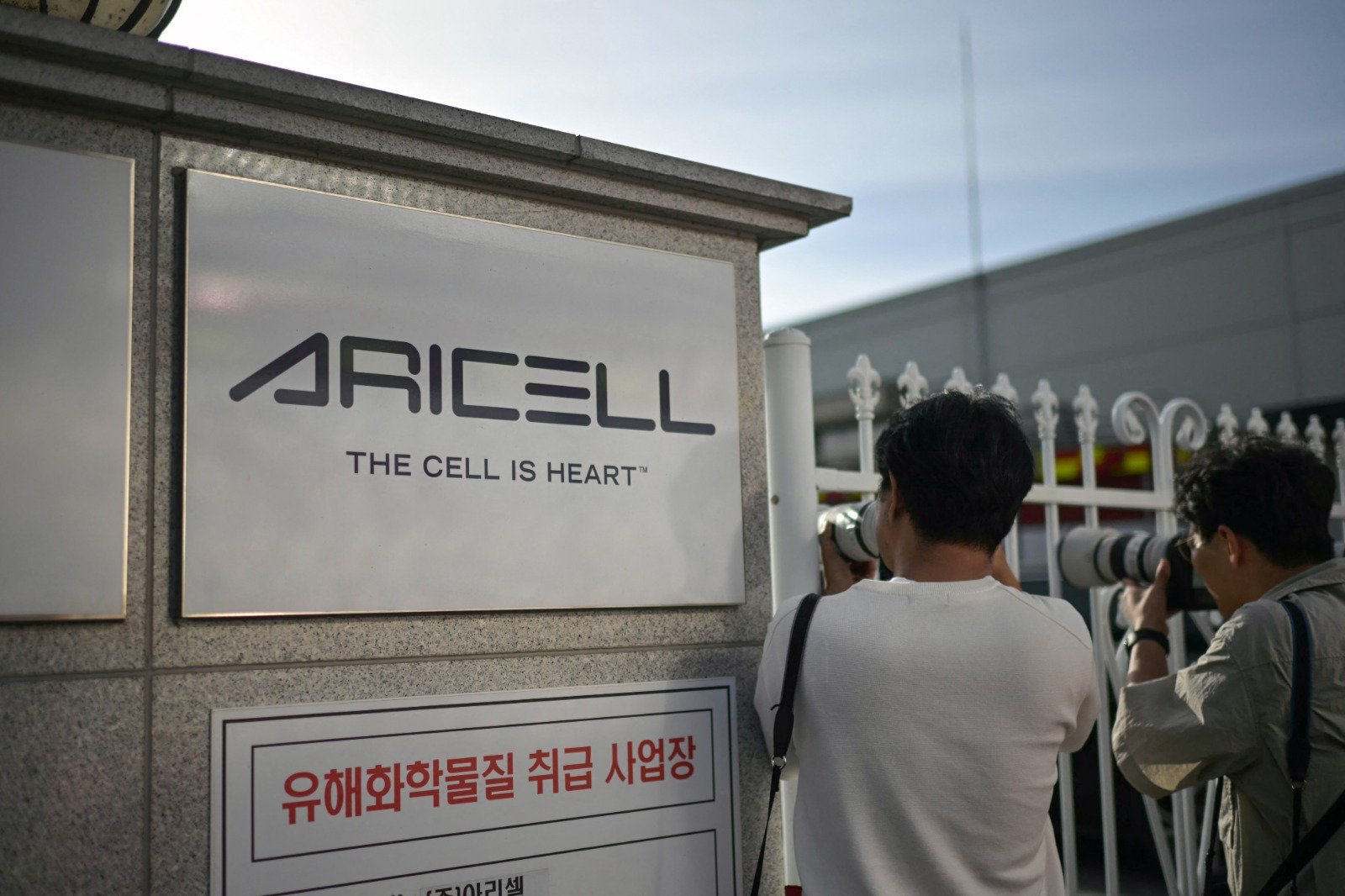 摄影师站在韩国电池制造商Aricell的标志旁边，拍著火灾现场照片。（图取自法新社）